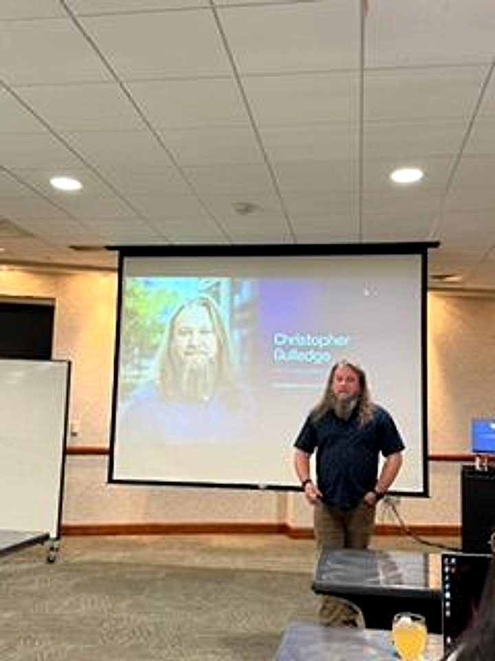 Christopher Gulledge standing beside a projected title slide bearing his name at the start of the Colorado River Valley Chamber workshop at Grand River Health in Rifle